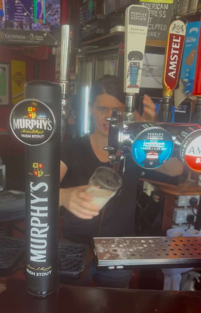 Murphy's Irish Stout beer tap at a pub, with a person pouring beer in the background.