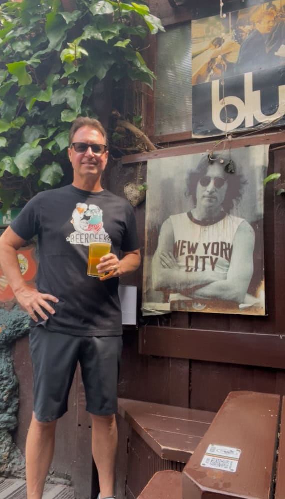 Beers enthusiast enjoying a beer at a pub, greenery, and art in the background.