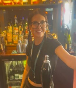 Beer bartender serving drinks at a lively bar, surrounded by an array of craft beers and liquor bottles.