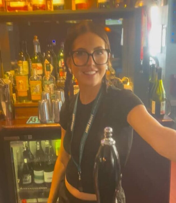 Beer bartender serving drinks at a lively bar, surrounded by an array of craft beers and liquor bottles.